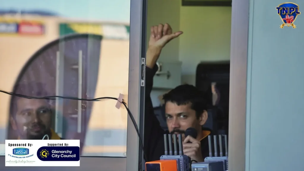 Commentator in the box behind glass, mid-call with hand raised