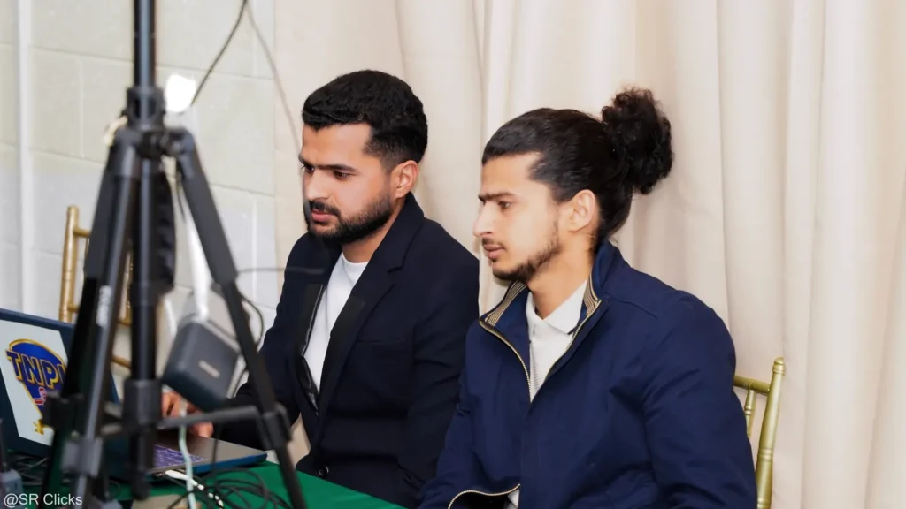 Two crew members seated beside a camera on a tripod