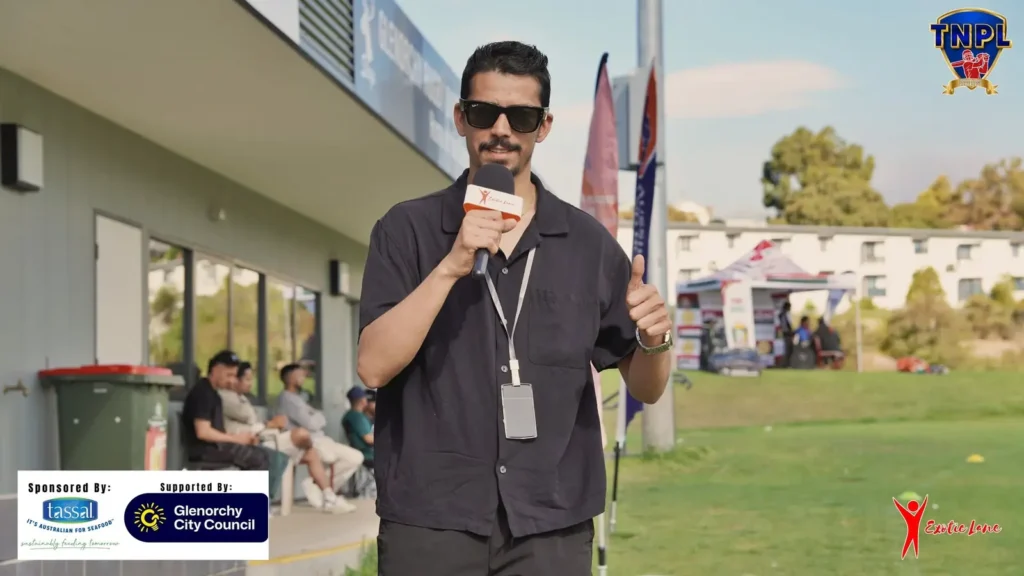 Presenter with a microphone and lanyard speaking to camera beside the ground