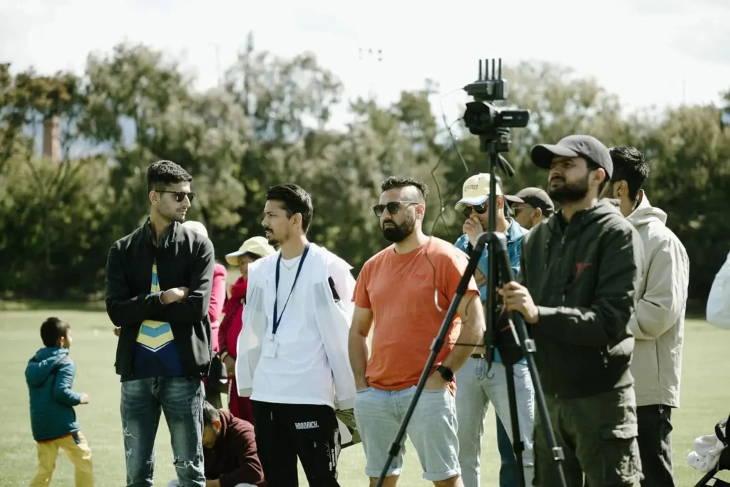 Crew and spectators beside a camera on a tripod at the sideline